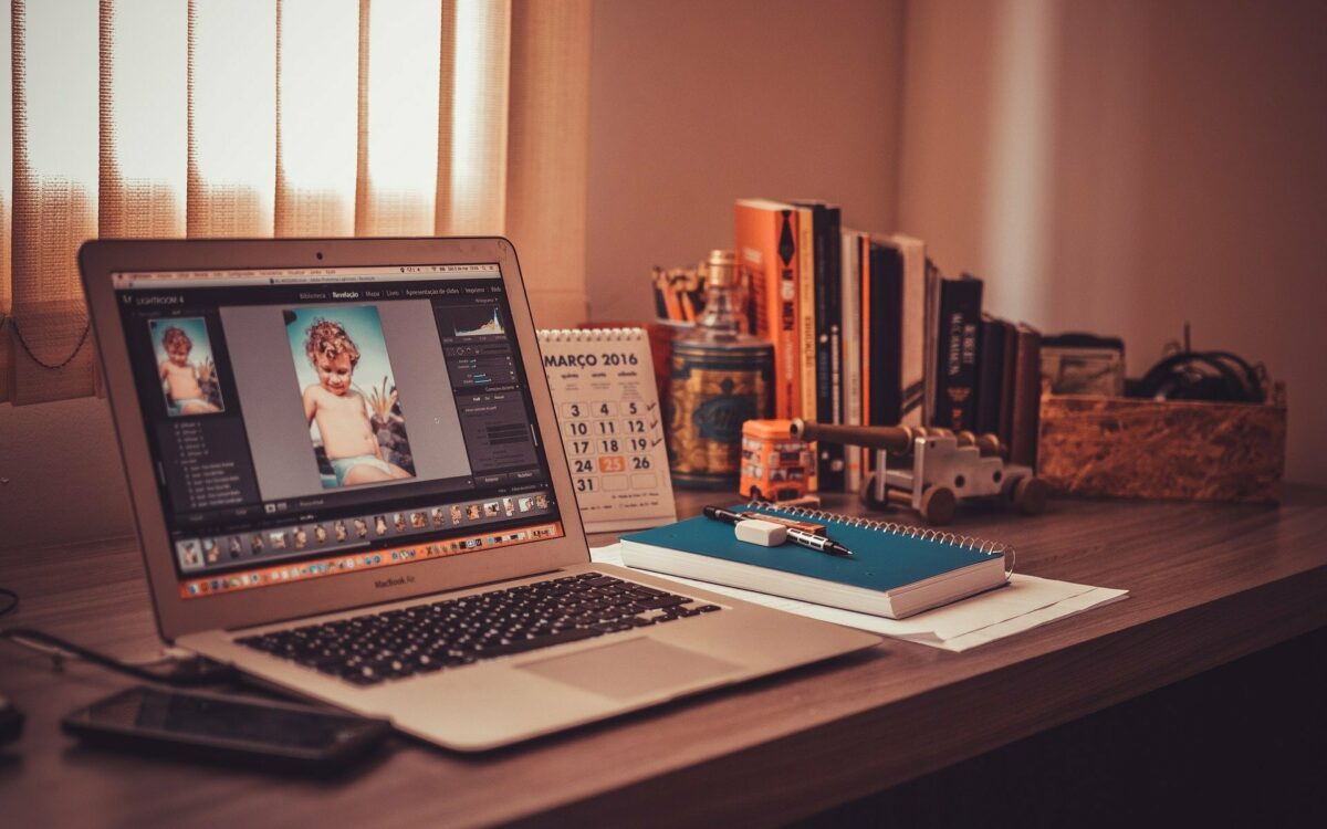Homeoffice Arbeitsplatz mit aufgeklapptem Laptop, Notizbuch, Tischkalender und Stiften, der Schreibtisch steht vor Fenster mit Jalousien Homeoffice Arbeitsplatz mit aufgeklapptem Laptop, Notizbuch, Tischkalender und Stiften, der Schreibtisch steht vor Fenster mit Jalousien